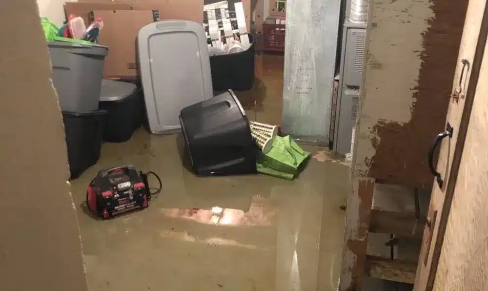 Sandy Utah Water Damage Restoration services from The Flood Co. A picture of standing water in a basement with plastic storage containers in the water.