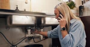 Technician inspecting a leaking pipe under a kitchen sink